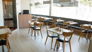 A modern dining area with wooden tables and chairs, a small counter with a computer, and large windows offering a view of the outdoors. - Hotel Las Lomas (Lima)