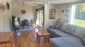 A living room with a wooden floor, a grey sofa, a wooden coffee table, a TV, and a dining area with a table and chairs.