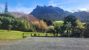 A gravel driveway leading to a wooden fence, with a mountain and lush greenery in the background.