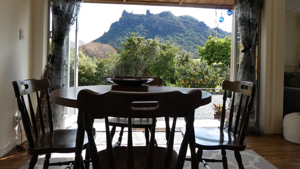 A dining area with a table and chairs, a view of a mountain, and a wooden ceiling.
