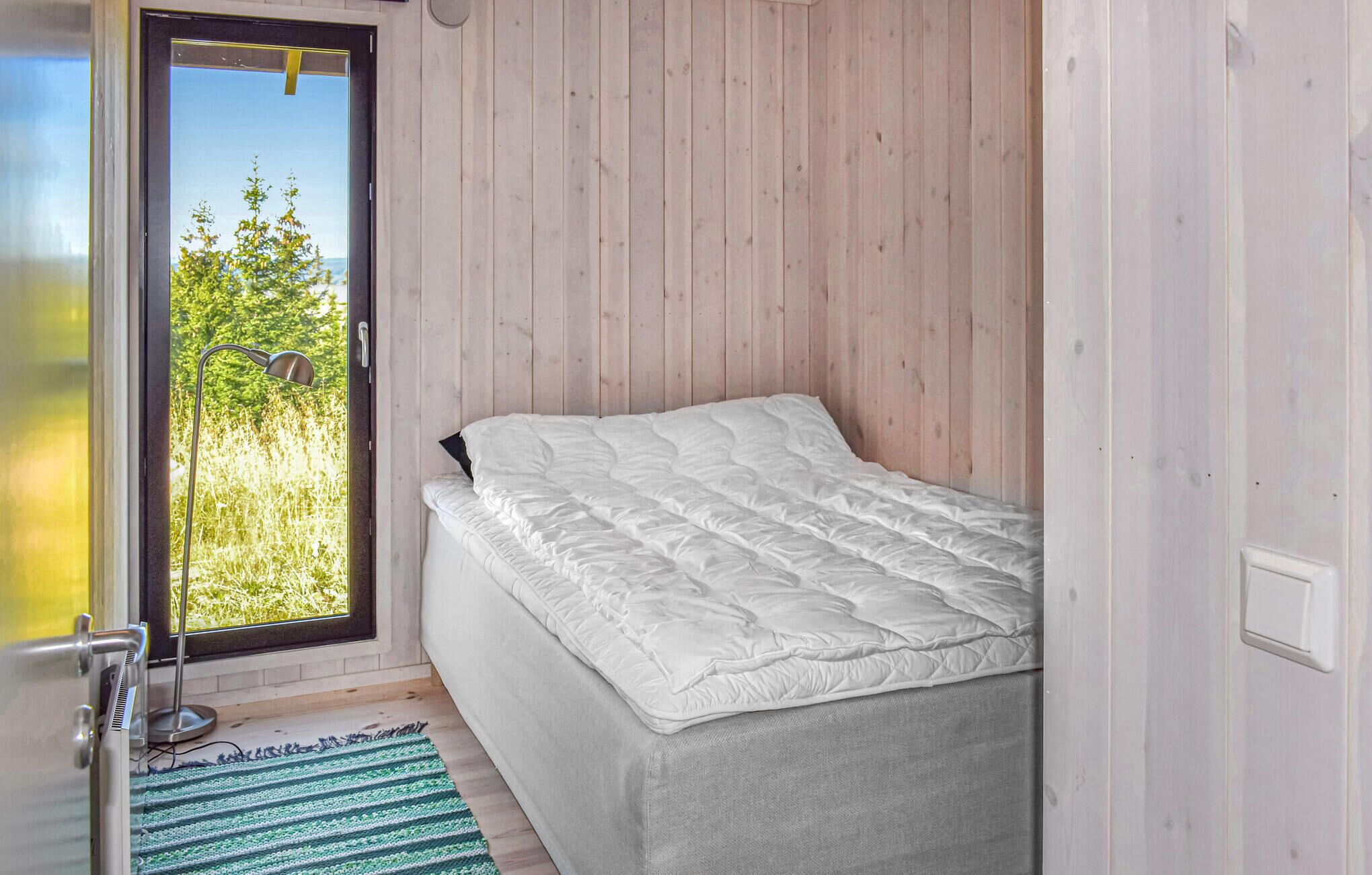 Une chambre avec un lit, une porte donnant sur un balcon et une vue sur la verdure.