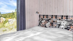 A bedroom with a bed, a headboard with a mosaic pattern, a window with a view of a forest, and a small wall-mounted lamp. - Beautiful home in øyer with sauna (Øyer)