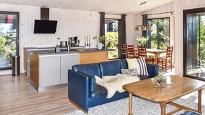 A modern kitchen with a central island, a dining area with a wooden table and chairs, a blue sofa, and a large window offering a view of greenery. - Beautiful home in øyer with sauna (Øyer)