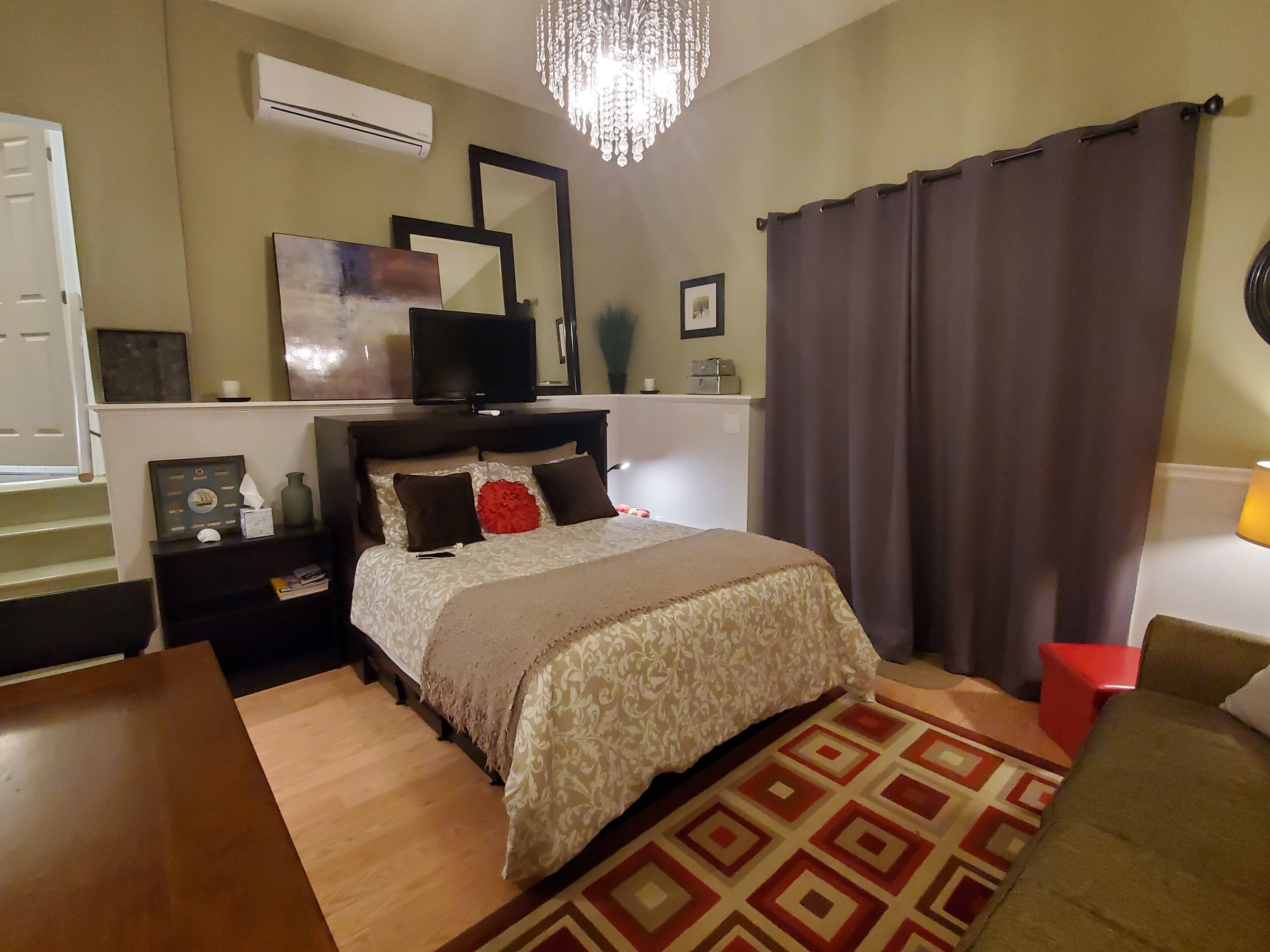 Una camera da letto con un letto, comodini, una TV, uno specchio e un lampadario.