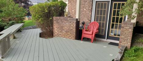 A wooden deck with a red chair and a bench, a brick wall, and a sliding glass door.