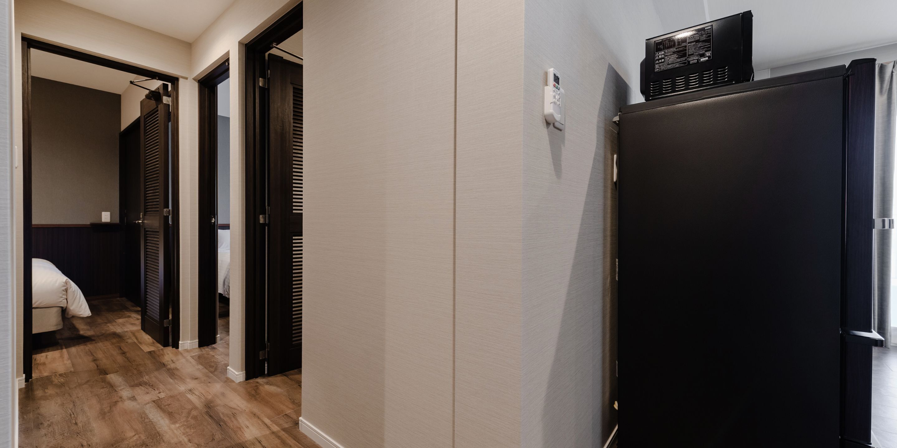 A hallway with a black refrigerator, a white wall, and a wooden floor.