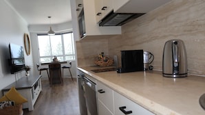 A modern kitchen with a dishwasher, a coffee maker, and a window with a view of trees. - Luxe Unit with 160 degree ocean and beach views (Alexandra Headland)