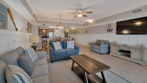 A spacious living room with a blue sofa, a wooden coffee table, and a TV on the wall. - ESCAPES1700sqft/updated/beachfront/Sleeps8 FREE BEACH SERVICE for 2-Mar-Oct (Orange Beach)