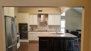 A kitchen with white cabinets, a stainless steel refrigerator, a built-in oven, a granite countertop, and a bar area with stools. - Quiet lakefront home. on Lake Leon, Eastland TX.  90 min to Fort Worth. (Eastland)