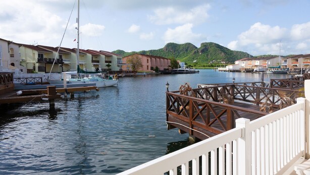 Ein Yachthafen mit vertäuten Booten, einer Holzbrücke und Gebäuden mit Balkonen mit Blick auf das Wasser.