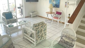Ein Wohnzimmer mit einer Couch, einem Sessel und einem kleinen Tisch. An der Wand hängt ein Fernseher, darüber ein Gemälde.