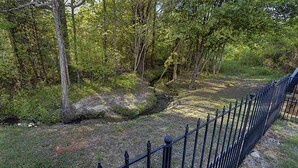 Un espace extérieur naturel agrémenté d’un pont en pierre, d’une clôture en métal et d’une végétation luxuriante.