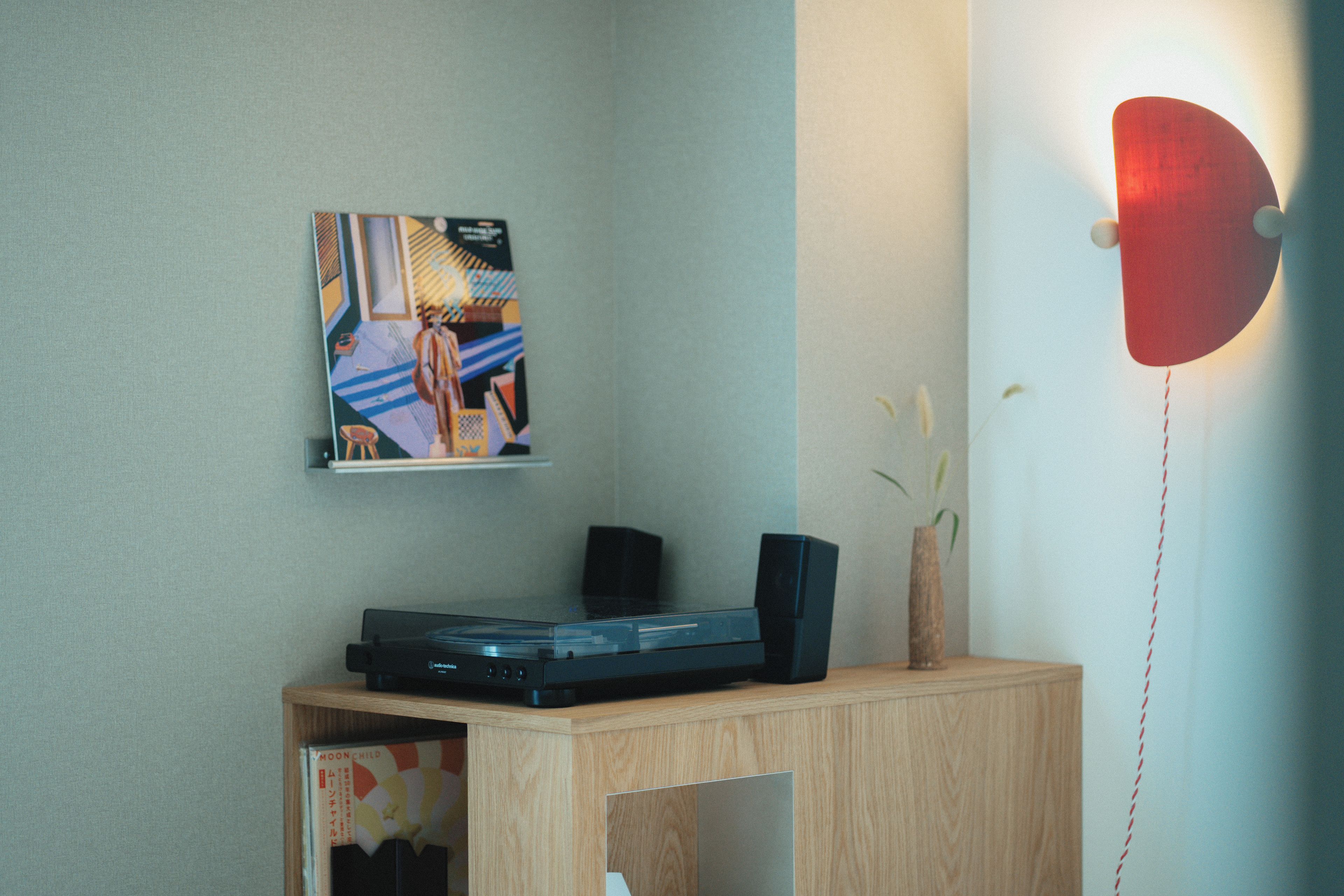 A room with a wooden desk, a black audio device, a wall-mounted picture, and a red light fixture.