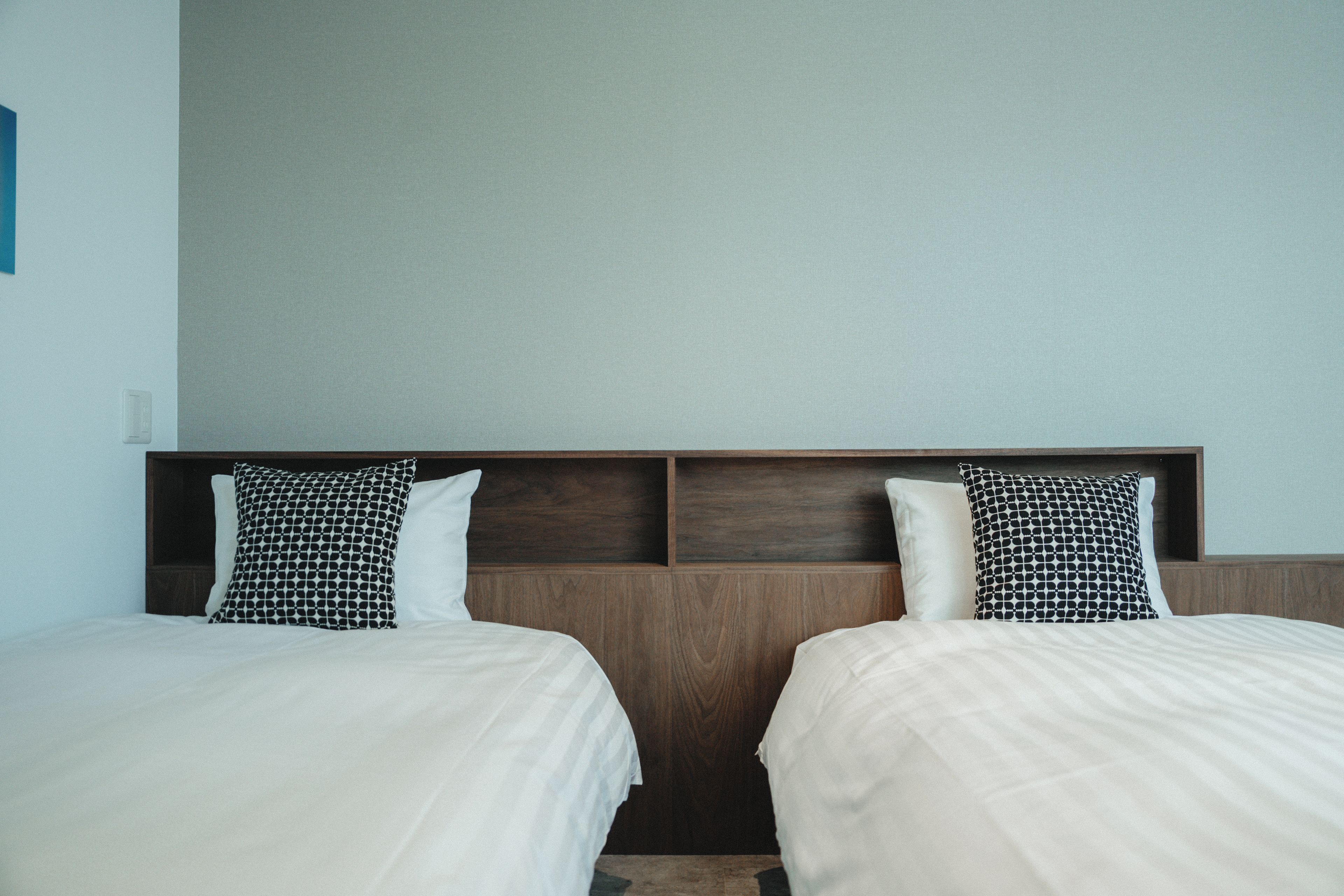 Habitación de hotel con dos camas, cada una con un cojín estampado y uno liso, y un cabecero de madera.
