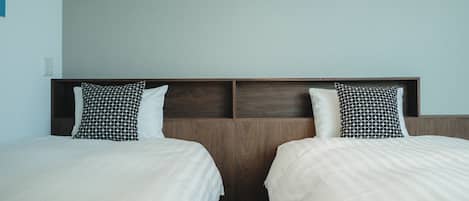 A hotel room with two beds, each with a patterned pillow and a plain pillow, and a wooden headboard.