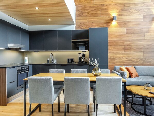 A modern kitchen with dark cabinetry, a wooden dining table, and grey upholstered chairs.