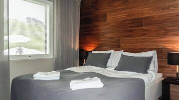 Habitación de hotel con cama, mesita de noche, lámpara, ventana con cortinas y pared de madera.
