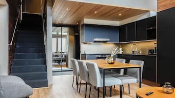 Une cuisine moderne avec des meubles de couleur sombre, une table à manger en bois et un escalier menant à l’étage supérieur.