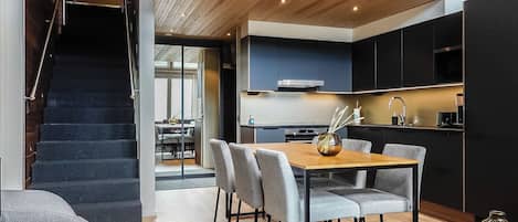 A modern kitchen with dark cabinets, a wooden dining table, and a staircase leading to an upper level.