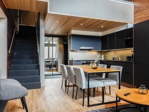 A modern kitchen with dark cabinets, a wooden dining table, and a staircase leading to an upper level.