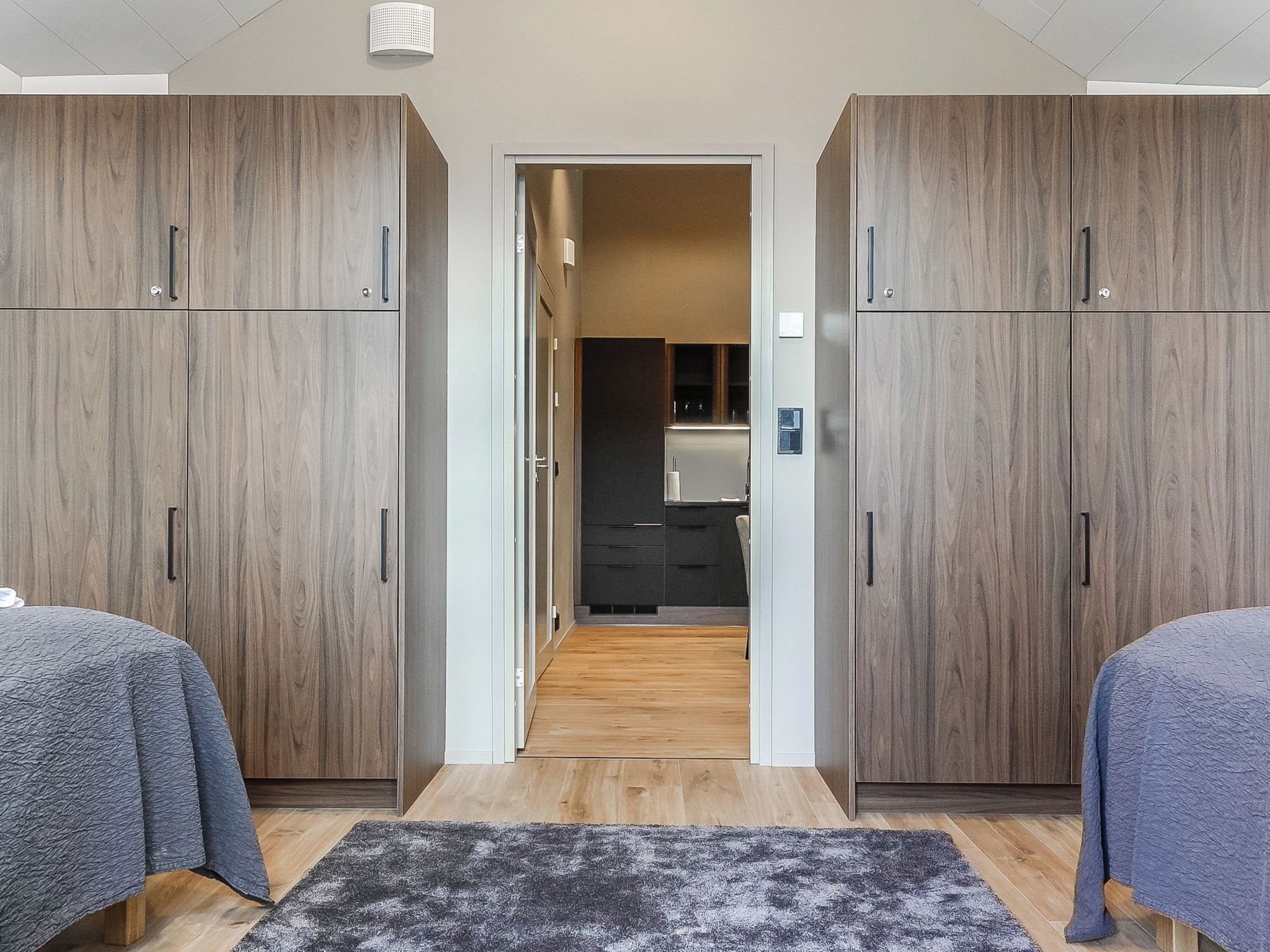 Une chambre moderne avec deux lits, un tapis de couleur sombre et des armoires en bois.