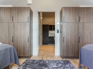 A modern bedroom with two beds, a dark-colored rug, and wooden wardrobes.