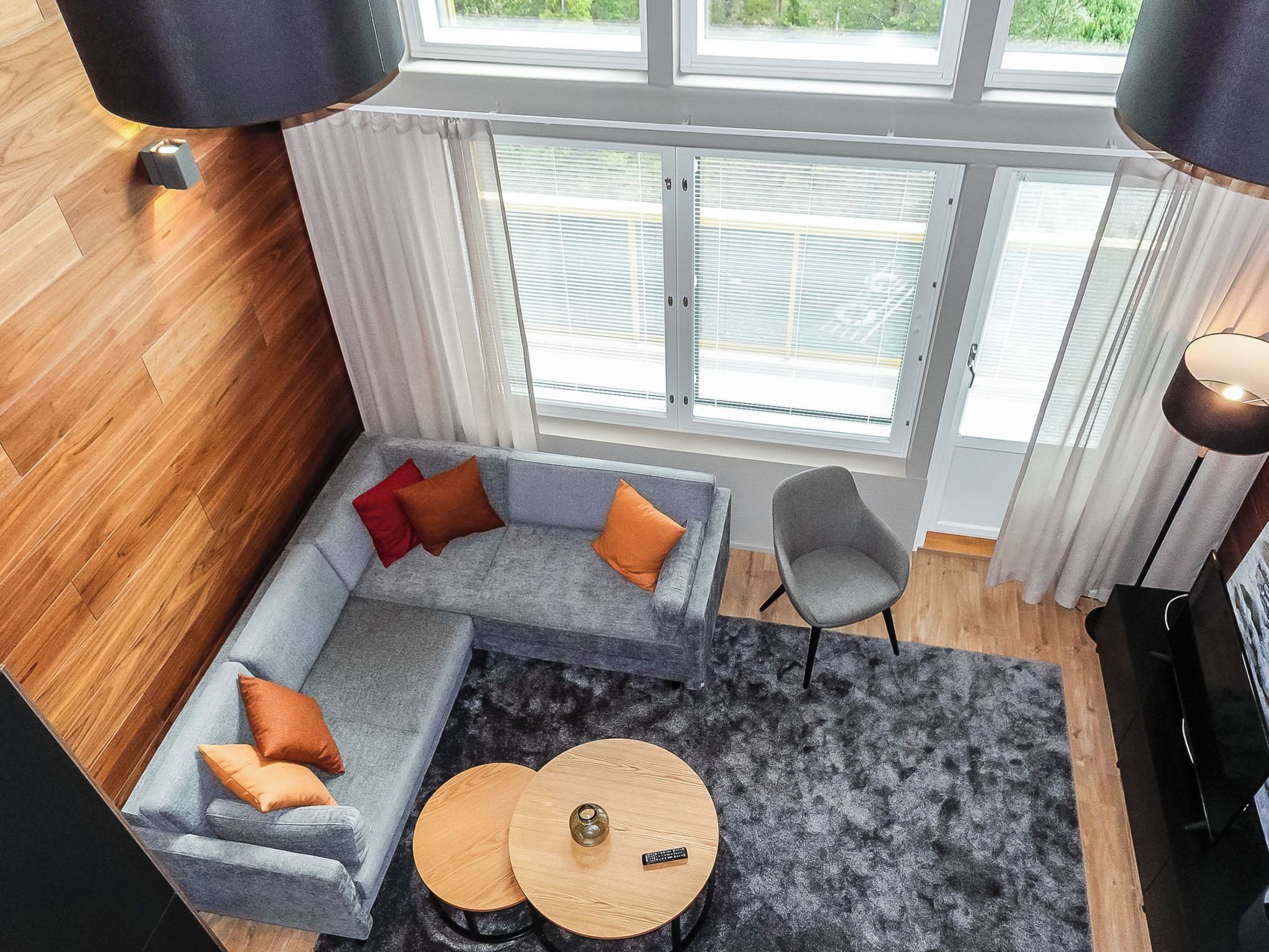 A modern living room with a grey sectional sofa, a round coffee table, a grey armchair, and a large window with blinds.
