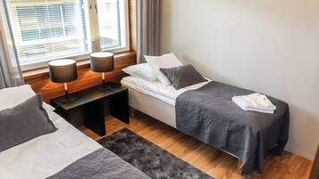 A hotel room with two beds, a window with blinds, a bedside table with lamps, and a rug.