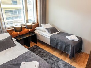 A hotel room with two beds, a window with blinds, a bedside table with lamps, and a rug.