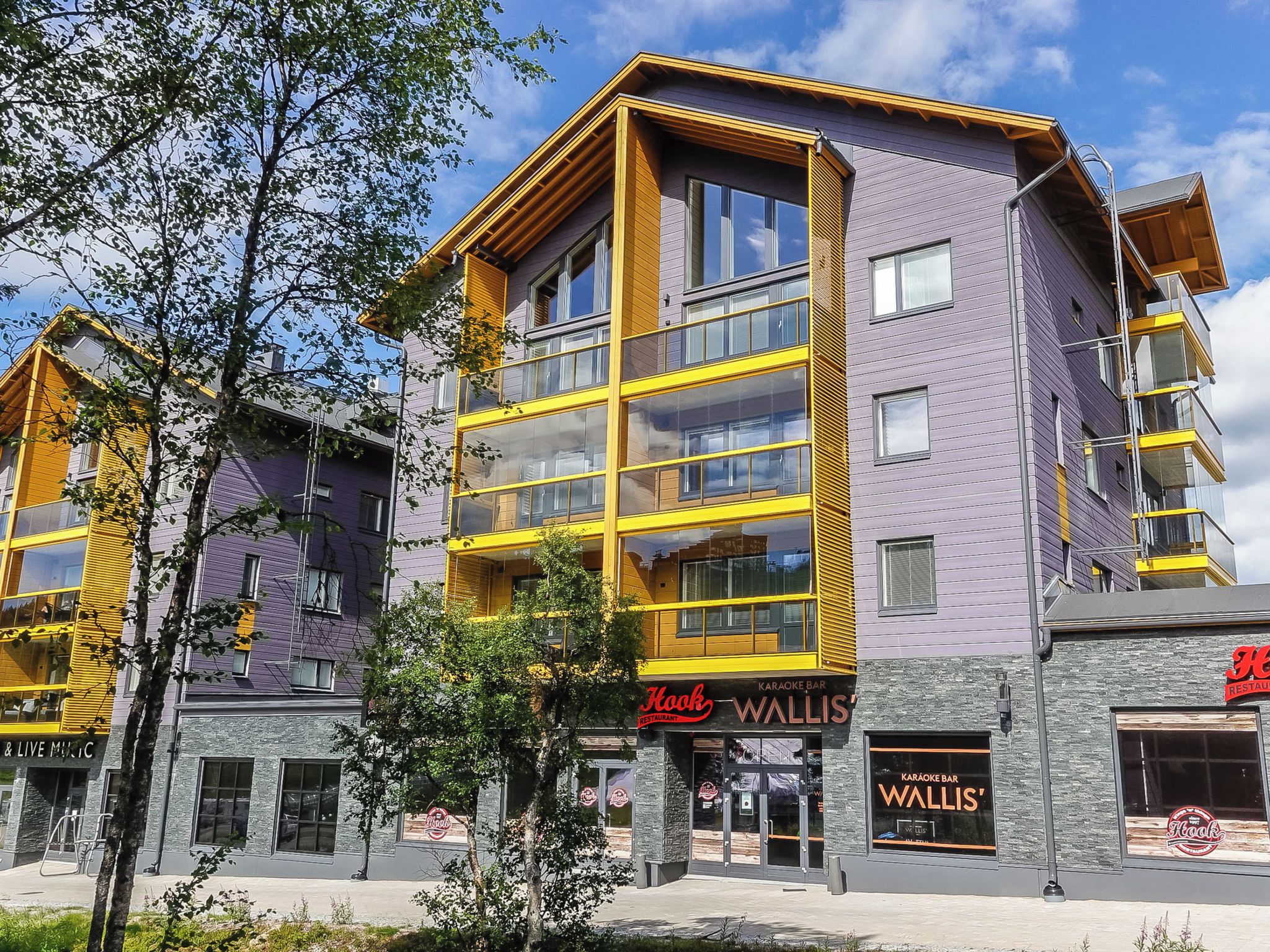 Un immeuble à plusieurs étages, doté d’une façade jaune et violette, qui abrite un restaurant appelé « Hook Restaurant » et un bar karaoké appelé « Wallis’ Karaoke Bar ».