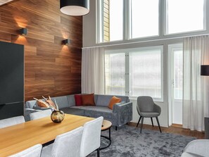 Un salon moderne avec un mur d’accent en bois, un canapé gris, une table à manger en bois et un fauteuil gris.
