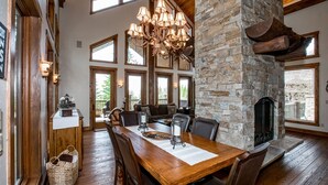 A dining area with a wooden table, chairs, a chandelier, stone walls, and a fireplace.