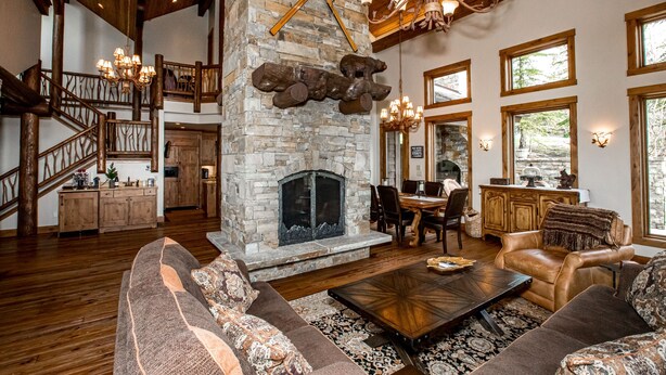 A spacious living area with a stone fireplace, wooden floors, and a staircase.