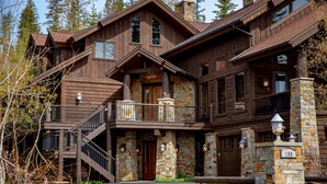 A large, multi-story log cabin with a stone foundation, multiple balconies, and a prominent front entrance.