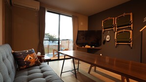 A modern living room with a sofa, a wooden dining table, and a TV mounted on the wall. - SORAPIA Villa Mt.Fuji Front (Fujikawaguchiko)