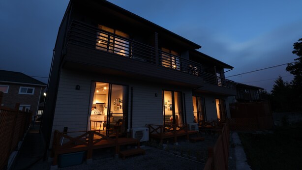 A two-story house with an open front door, a balcony, and a patio area with benches. - SORAPIA Villa Mt.Fuji Front (Fujikawaguchiko)