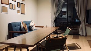 A modern living room with a wooden dining table, a blue sofa, and a green chair. There are framed pictures on the wall and an air conditioning unit above the sofa. - SORAPIA Villa Mt.Fuji Front (Fujikawaguchiko)