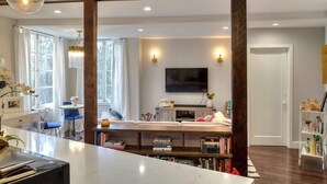A modern living room with a large TV, wooden beams, a dining area with a table and chairs, and a bookshelf. - Amazing Apartment attached to historic home in Pasadena! (Pasadena)