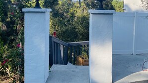 A gated entrance with two ornate street lamps, a white wall, and a metal gate. - Amazing Apartment attached to historic home in Pasadena! (Pasadena)