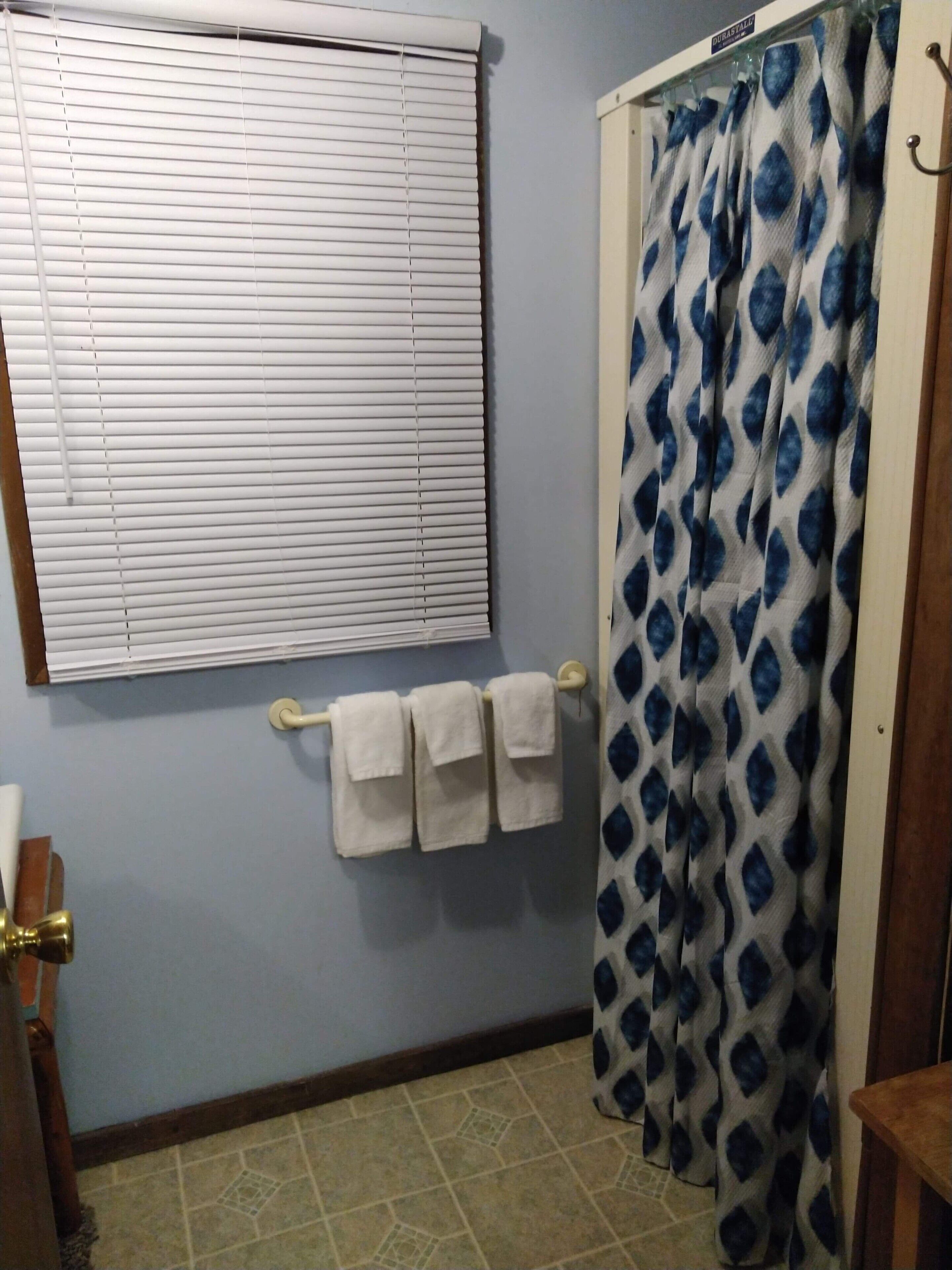 Une salle de bain avec une fenêtre, un rideau de douche et un porte-serviettes avec trois serviettes.