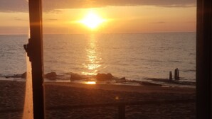 A sunset over the ocean viewed through a window with a metal frame. - #6 Two bedroom Dog friendly beachfront cabin. (Au Sable Township)