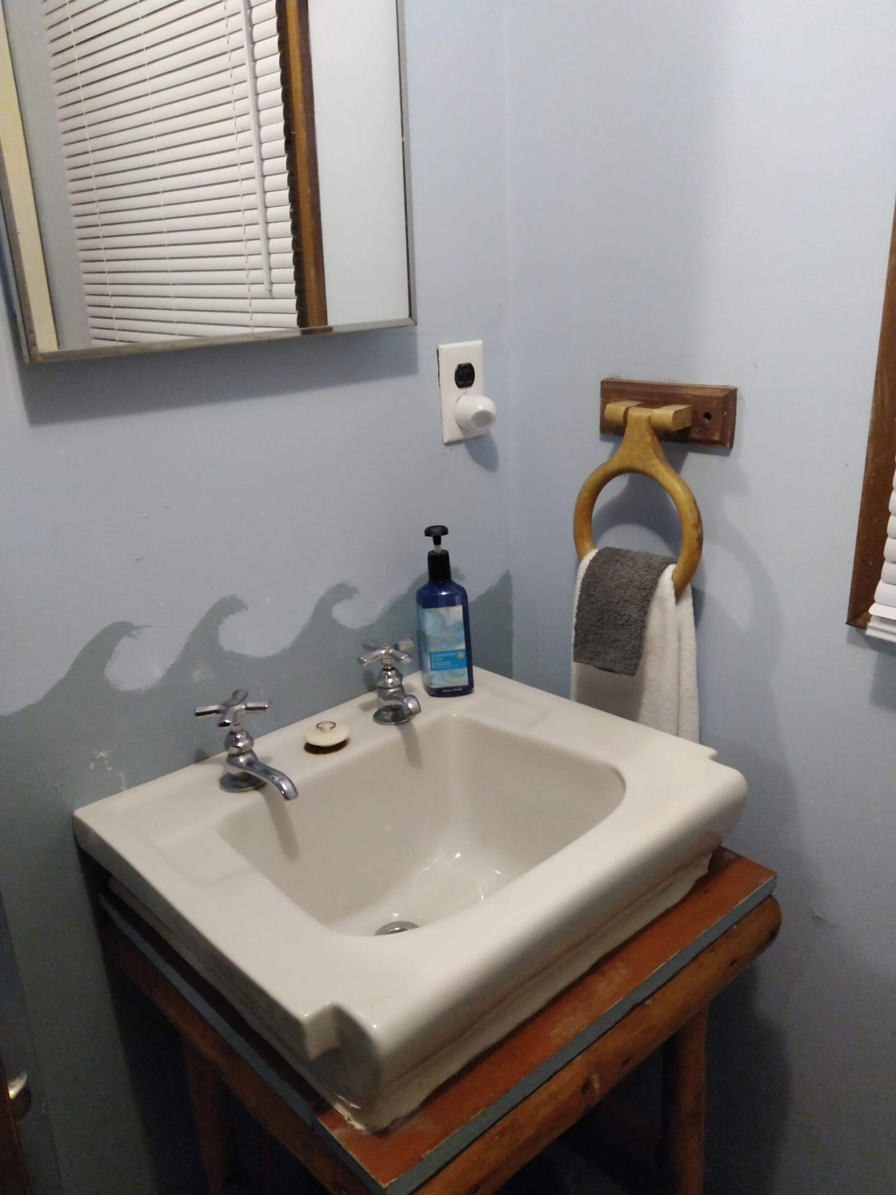 A bathroom with a white sink, a mirror, a towel rack, and a soap dispenser.