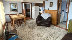 A living room with a sofa, a dining table, and a kitchen area in the background. - #6 Two bedroom Dog friendly beachfront cabin. (Au Sable Township)