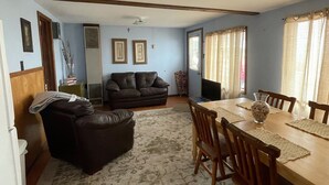A spacious living room with a large wooden dining table, a leather sofa, and a patterned rug. - #6 Two bedroom Dog friendly beachfront cabin. (Au Sable Township)