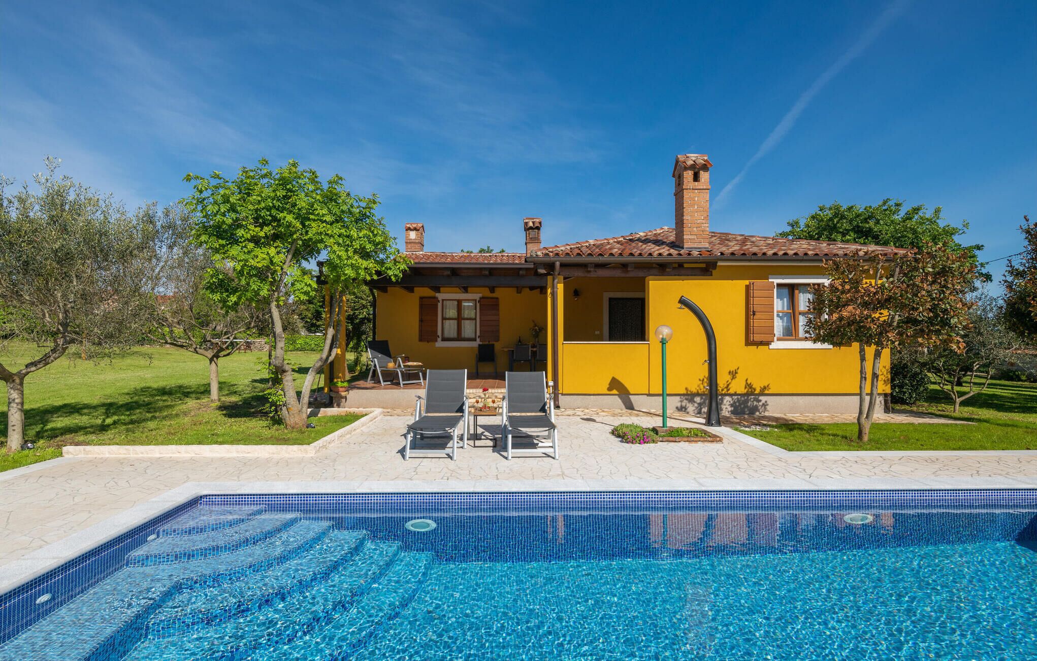 A yellow villa with a swimming pool, outdoor seating, and a garden.