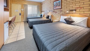 A hotel room with two beds, a desk, a chair, a television, and a brick wall with a picture. - Roma Mid Town Motor Inn (Roma)