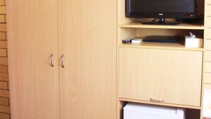 A room with a wooden wardrobe, a television on a shelf, and a small white appliance. - Roma Mid Town Motor Inn (Roma)