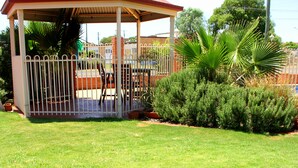 A gazebo with a red roof and white railing, surrounded by a well-maintained lawn and various shrubs. - Roma Mid Town Motor Inn (Roma)