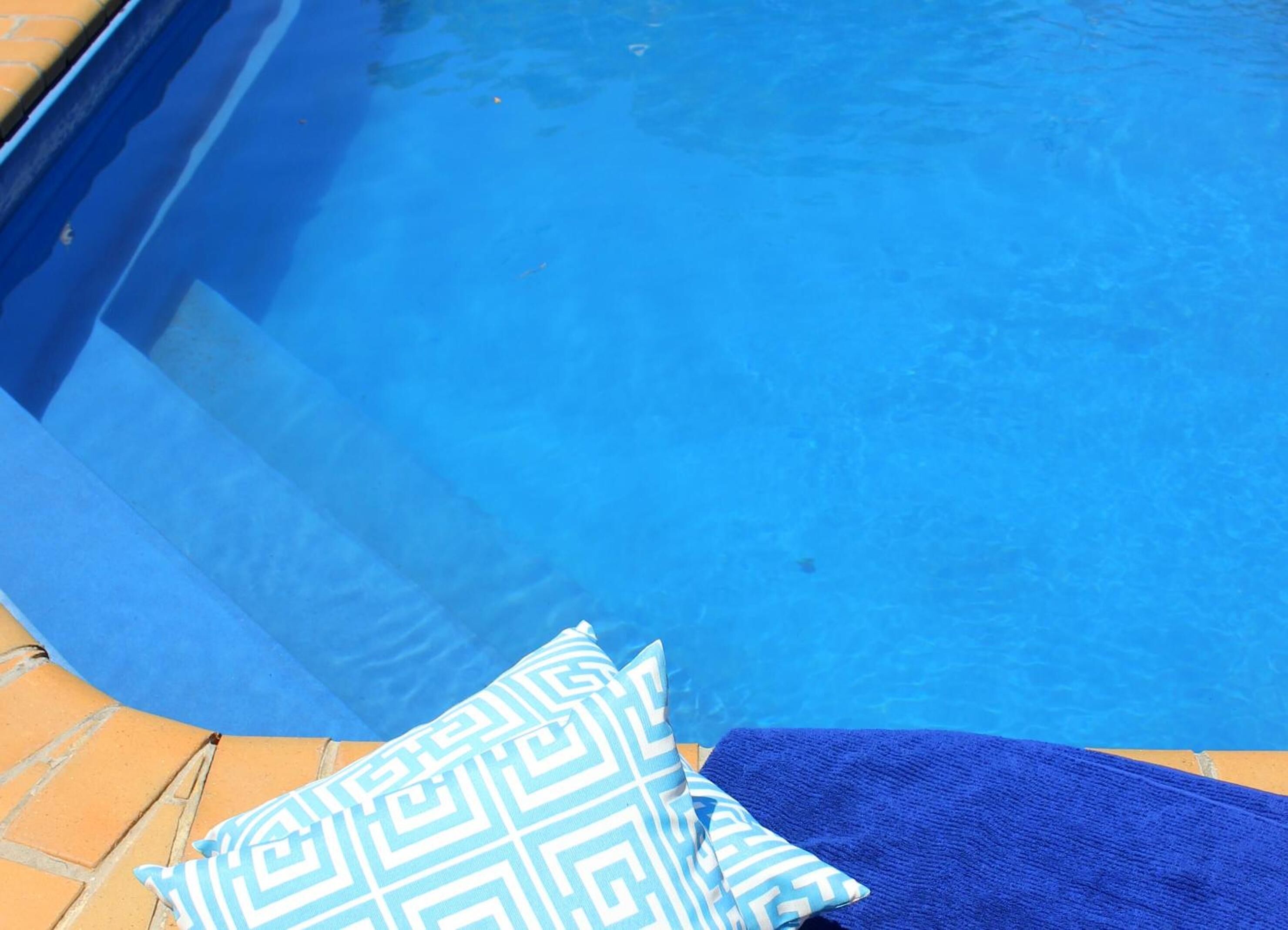 A pool with a blue edge and a blue towel and patterned pillow on the side.