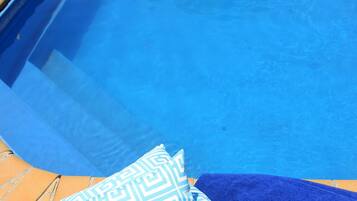 A pool with a blue edge and a blue towel and patterned pillow on the side.